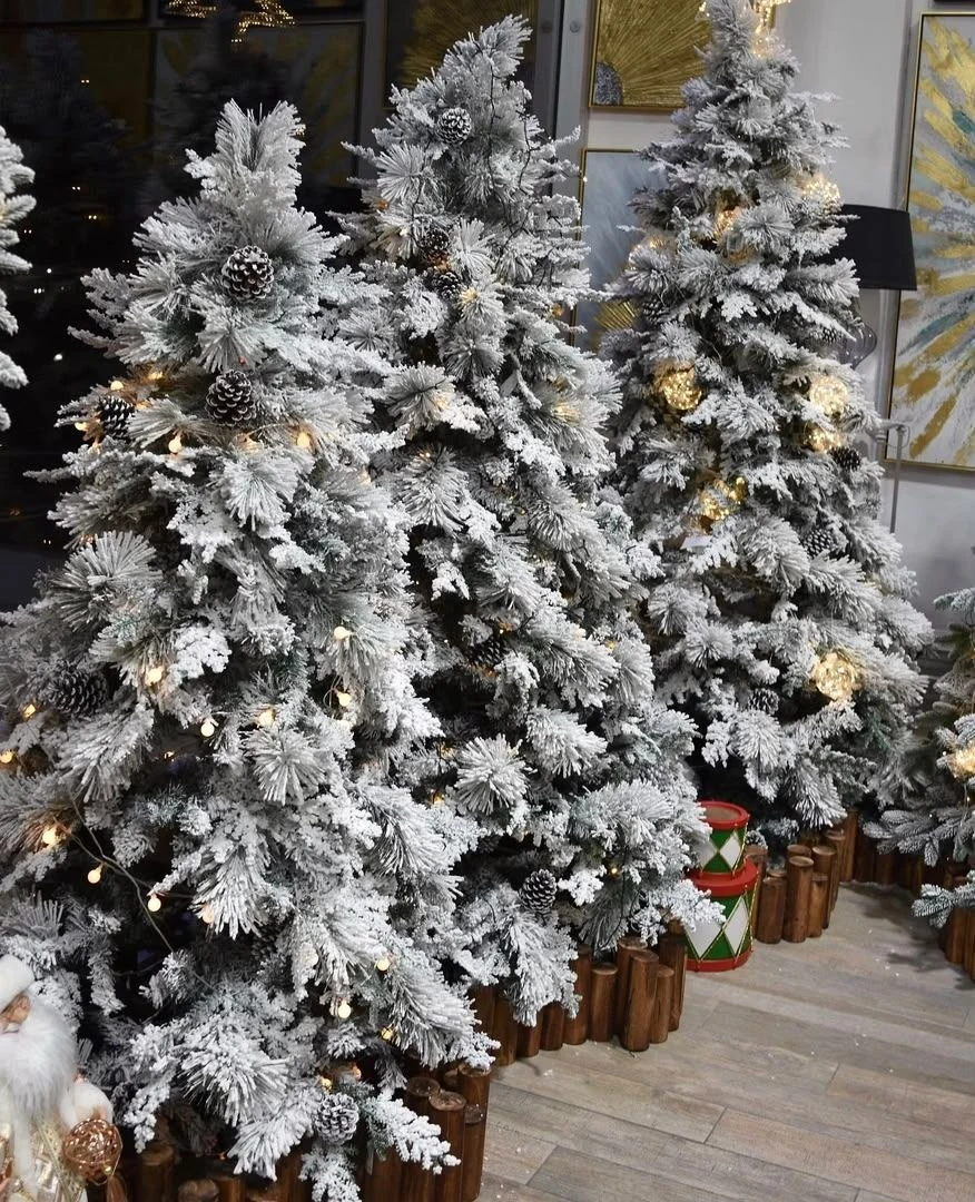 Snow-flocked artificial pine tree with pinecones and warm lights in an indoor display.